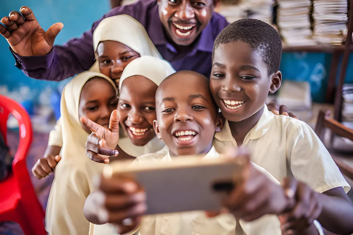 A teacher and four smiling schoolchildren sharing a phone in a classroom