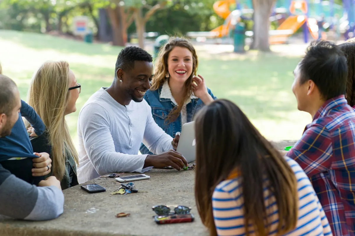Friends laughing together around a table in a park