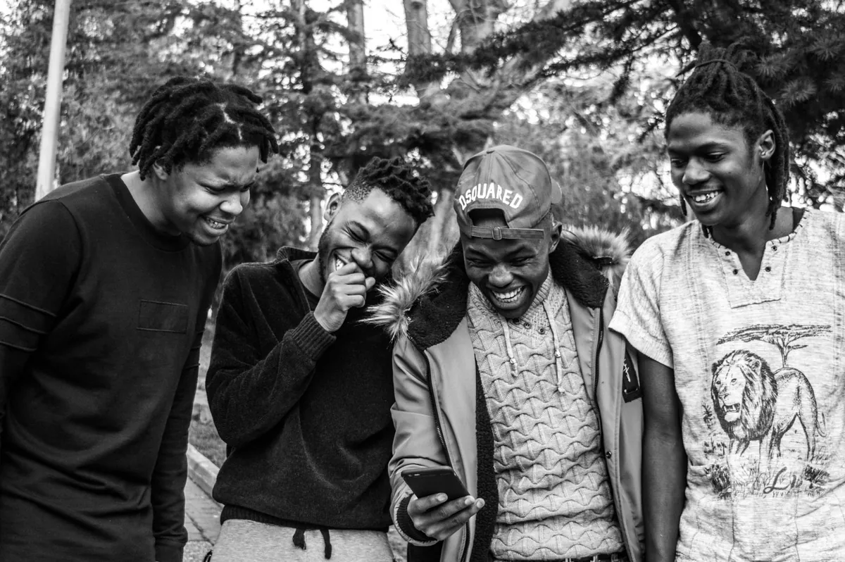 Four young men laughing together over a phone, in black and white